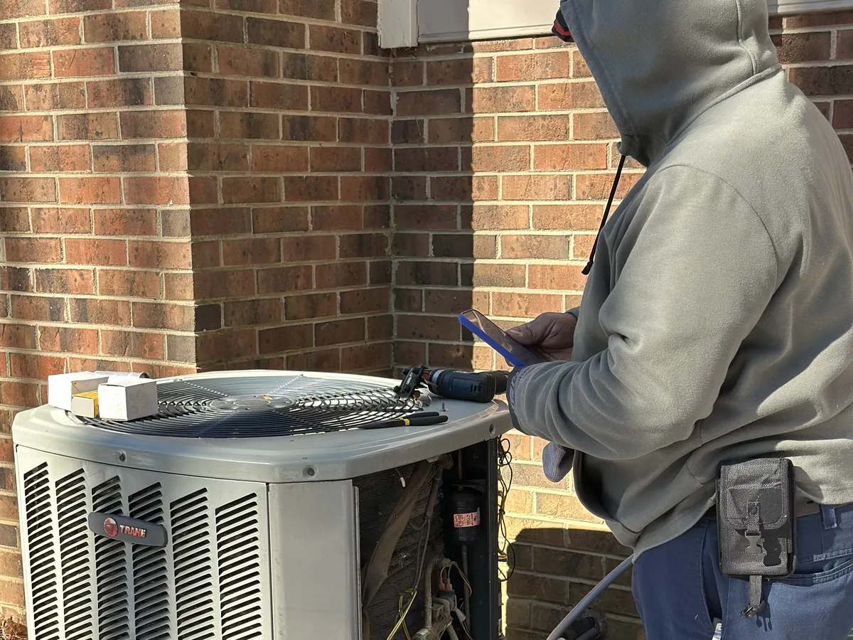 HVAC technician repairing an outdoor AC condenser unit with open panel showing internal components