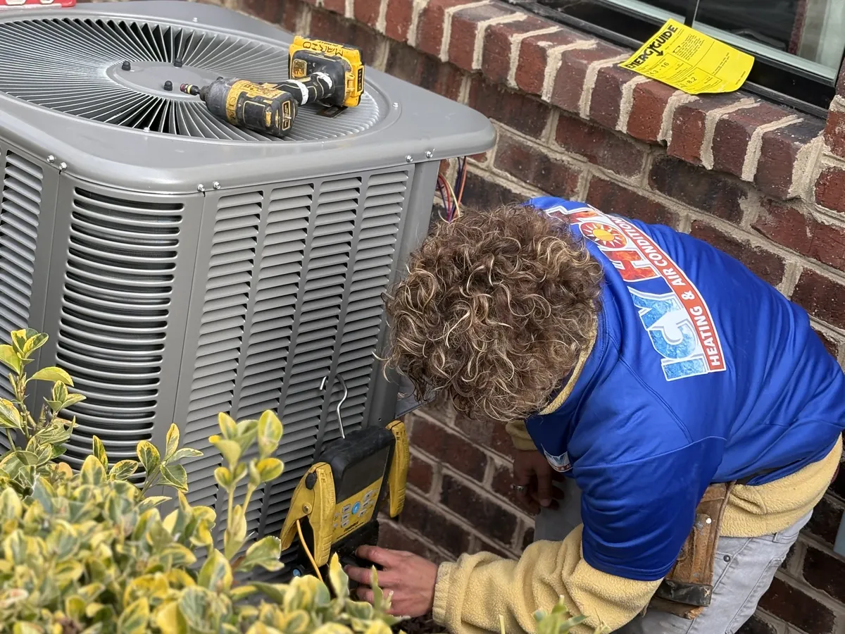 Icy Hot Heating and Air Conditioning technician installing an outdoor AC condenser unit beside a brick home