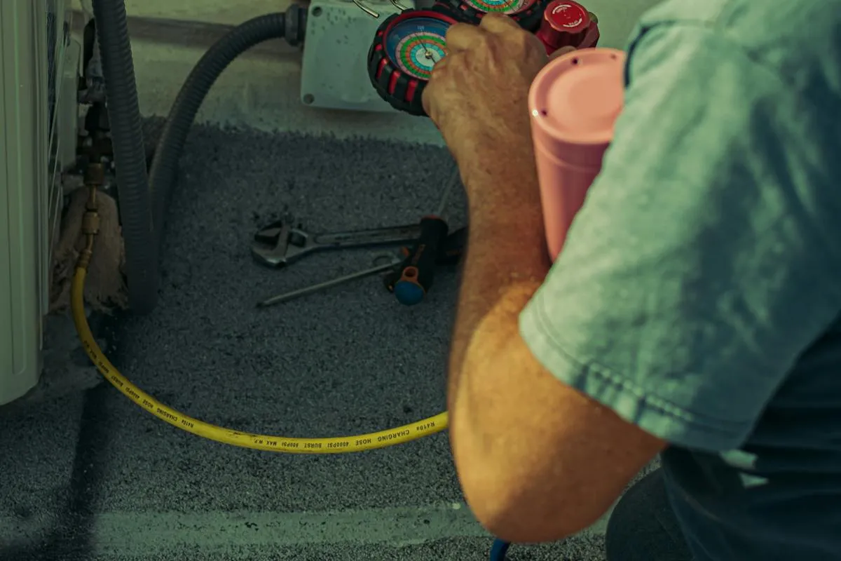 HVAC technician checking refrigerant levels on outdoor AC unit with manifold gauges