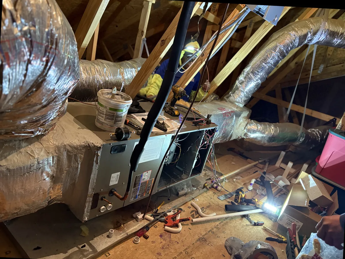 New furnace and air handler being installed in a residential attic with ductwork connections and professional tools
