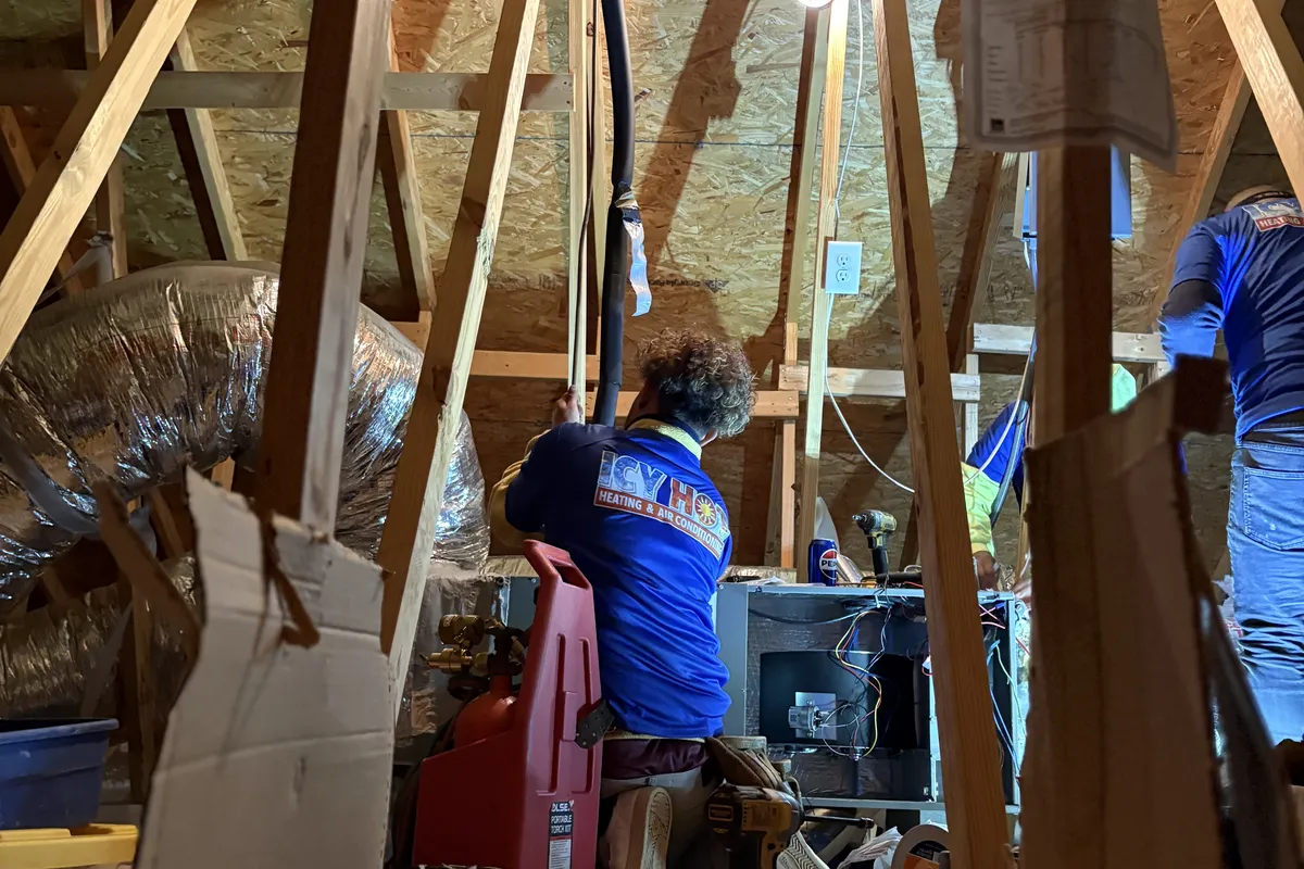 Two Icy Hot Heating and Air Conditioning technicians installing a heating system and air handler in a residential attic