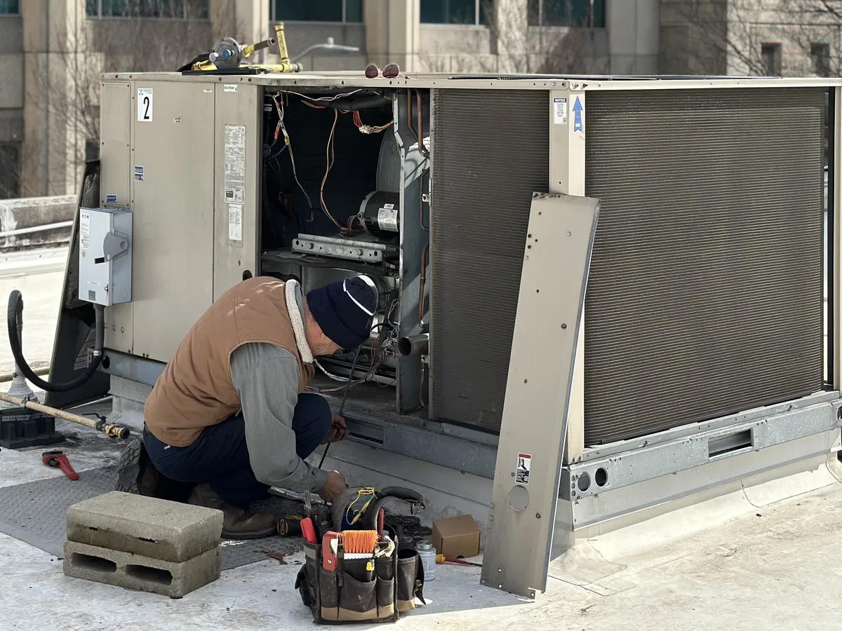 HVAC technician inspecting and servicing a commercial rooftop package unit with tools