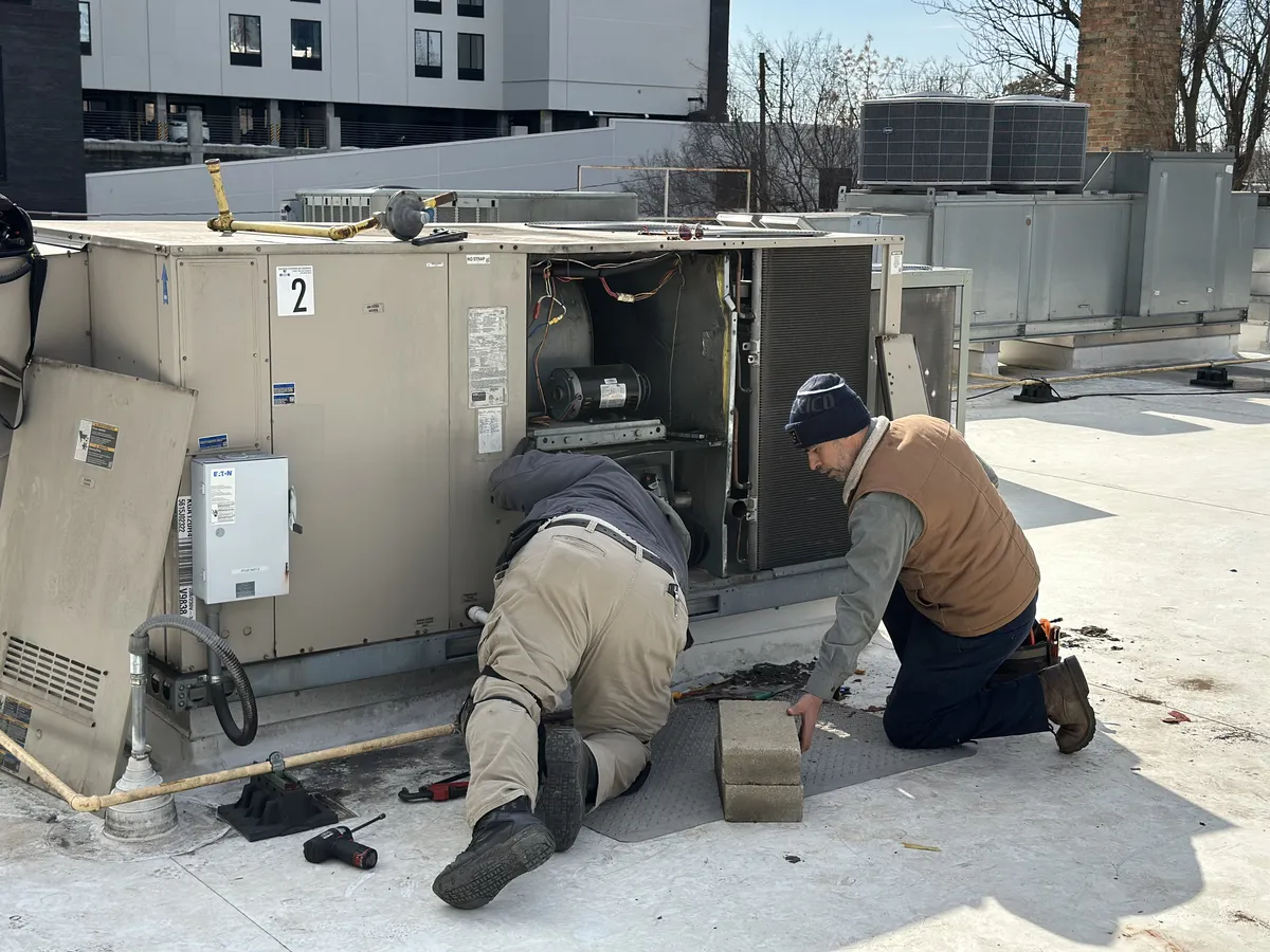 Two HVAC technicians performing maintenance on a commercial rooftop package unit with Eaton electrical panel