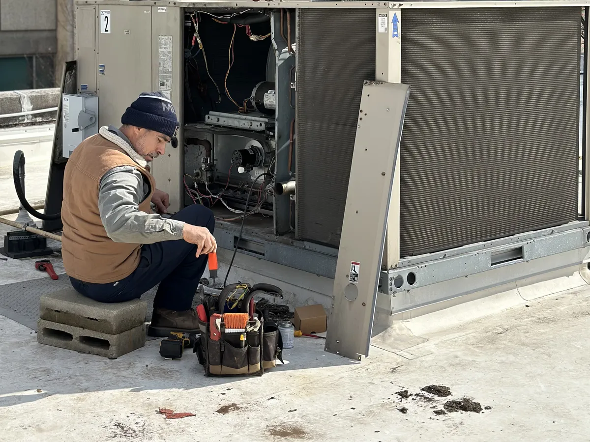HVAC technician with tool bag performing a tune-up on a commercial rooftop HVAC package unit
