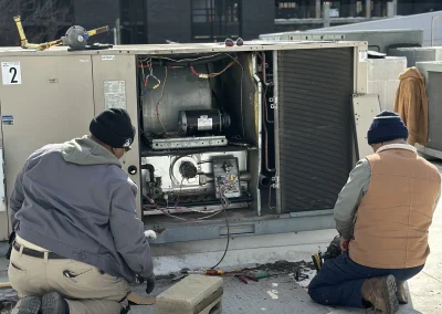 Two Icy Hot technicians kneeling beside open commercial rooftop HVAC unit performing repairs