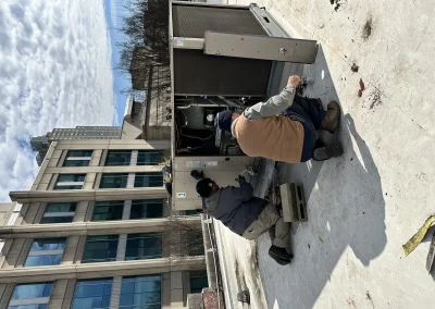 Two technicians servicing large commercial rooftop package HVAC unit