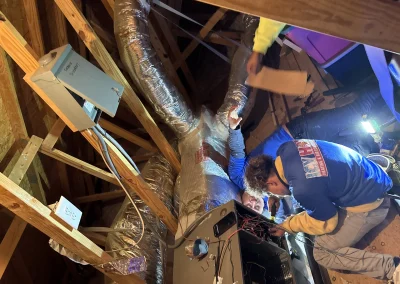 Icy Hot technician in blue shirt inspecting ductwork and HVAC equipment in attic