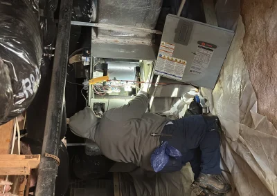 Technician repairing furnace wiring in crawl space with panel open