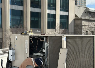 HVAC technician crouching beside open rooftop unit with tools