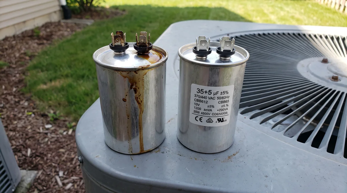 Side by side comparison of two AC dual-run capacitors on a condenser cabinet, the left one failed with brown dielectric oil weeping down the can and a scorched terminal, the right one new with a legible 35 plus 5 microfarad 370 slash 440 volt rating label